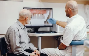 Dentist explaining dental implant treatment plan to patient using digital screen in clinic